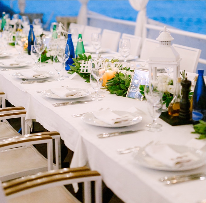 long wedding dinner table reception overlooking the sea with flower arrangement in the center of the table
