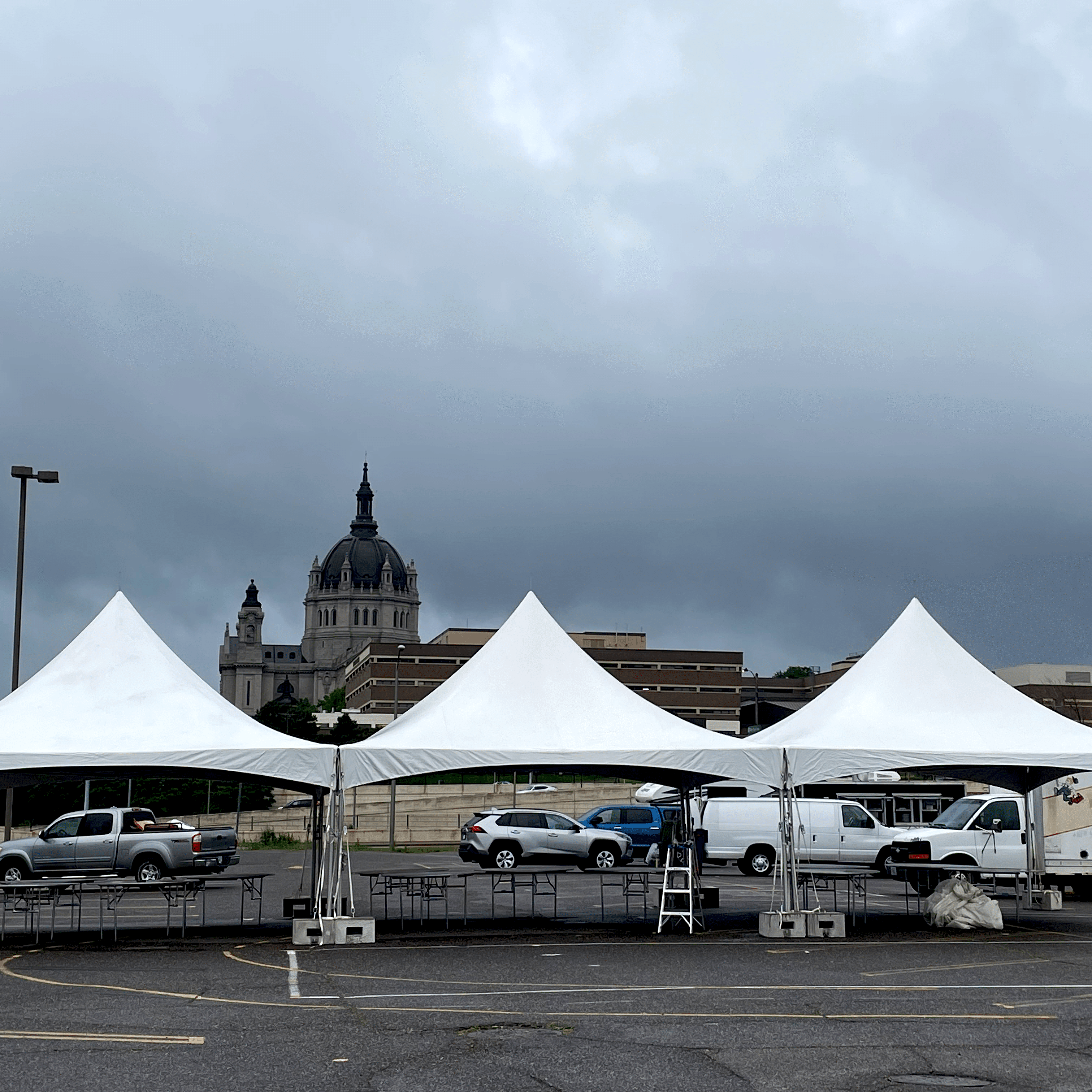 A three tent setup in a parking lot beneath dark, stormy clouds